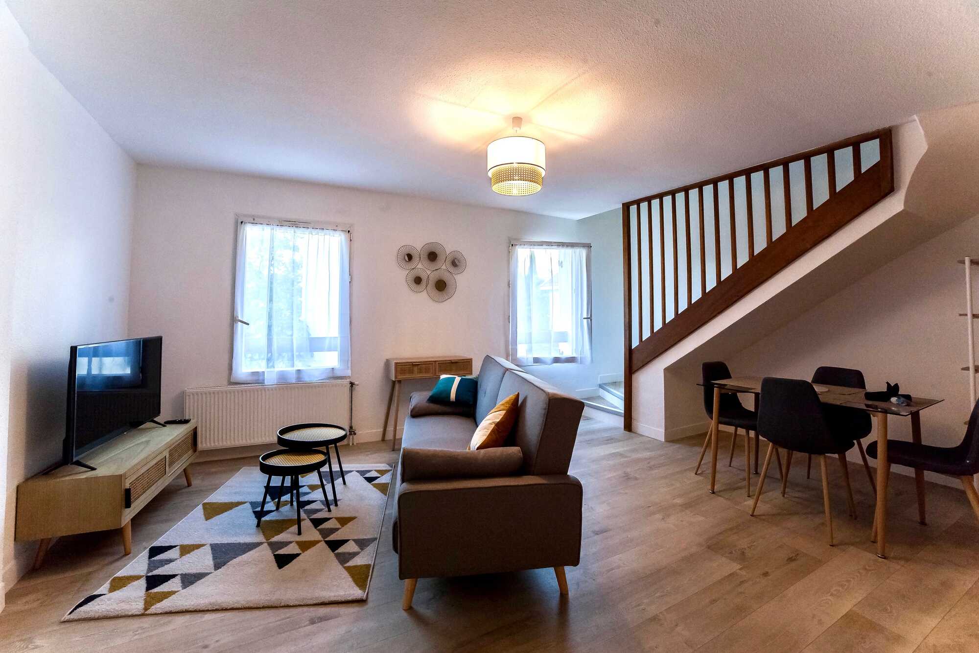Aménagement d’un salon scandinave et salle à manger à Limoges – VBN Salon rénové à Limoges par VBN : parquet bois clair, canapé moderne, tapis géométrique, escalier en bois et salle à manger intégrée.